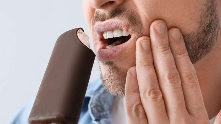 Persona sintiendo sensibilidad dental al tomar una bebida fría.