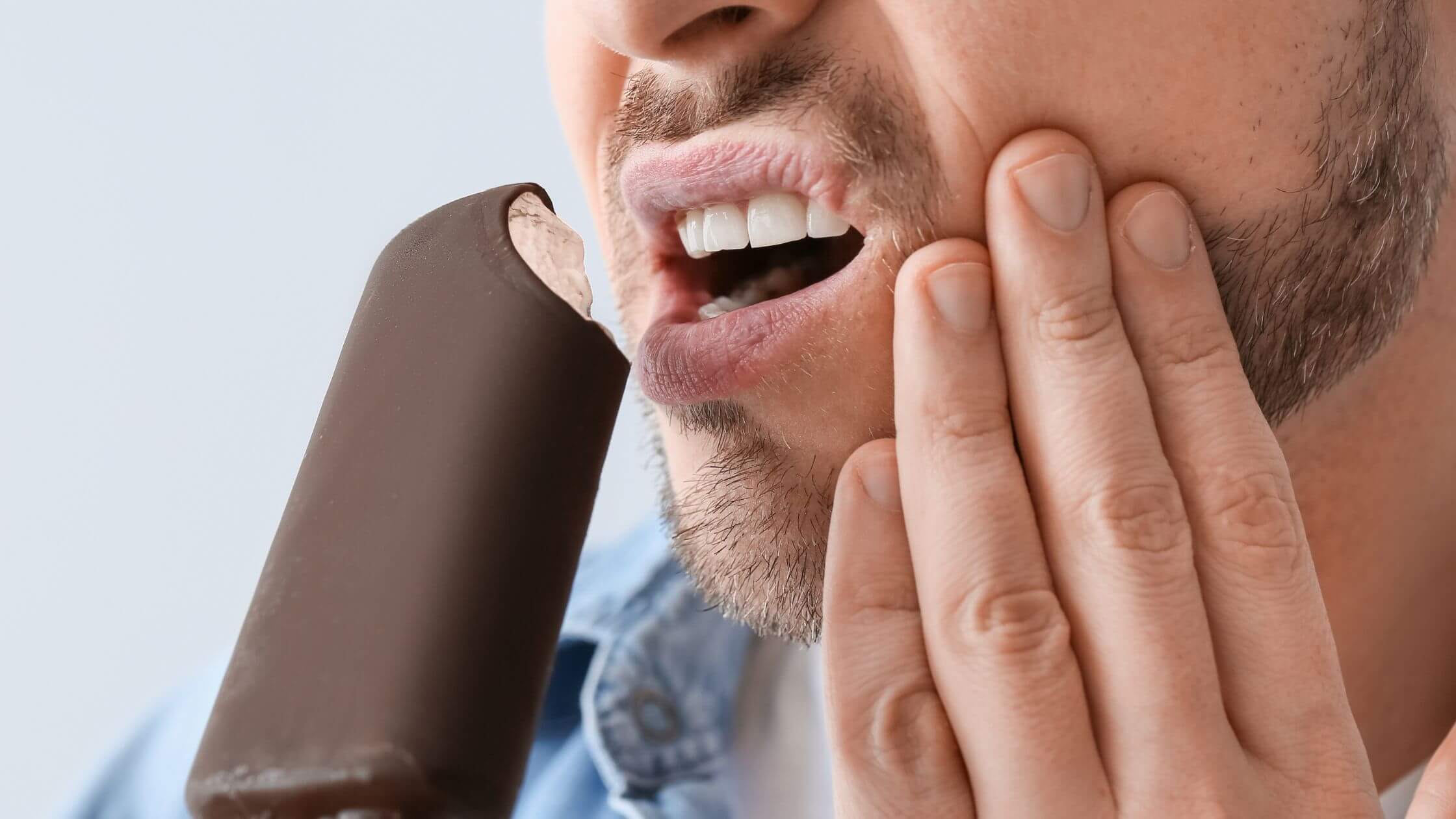 Persona sintiendo sensibilidad dental al tomar una bebida fría.